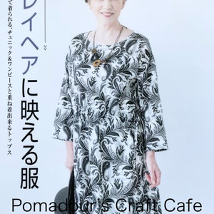 Könnte beinhalten: Eine Frau trägt ein langärmeliges Kleid mit Paisley-Muster in Schwarz und Weiß. Das Kleid hat einen runden Ausschnitt und eine lockere Passform. Der Text "Grey hair to look good" ist in japanischer Schrift auf der linken Seite des Bildes zu sehen. Der Text "Pomadour's Craft Cafe" ist in Schwarz und Weiß am unteren Rand des Bildes zu sehen. Der Text "mit einem Booklet" ist in japanischer Schrift auf der rechten Seite des Bildes zu sehen.