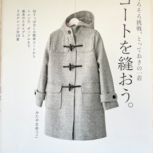 Puede incluir: Una portada de libro con un abrigo gris con botones negros y una percha blanca. El título del libro es "Costura de abrigo" en japonés. El libro trata sobre la costura de abrigos.