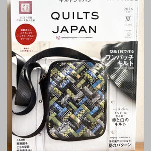 Może przedstawiać: Wydanie magazynu Quilts Japan z lipca 2026 roku, tom 206, z okładką przedstawiającą małą, prostokątną torebkę na ramię z tkanego materiału z czarnym paskiem. Torebka ma wielokolorowy wzór patchworkowy w odcieniach niebieskiego, zielonego i czarnego.