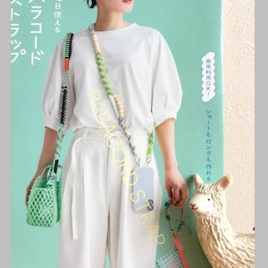May include: A multi-colored paracord strap featuring woven green, white, and grey patterns with wooden beads. The strap is attached to a light blue smartphone case and a small green lattice-style bag. Text on the image includes PARACORD STRAP.