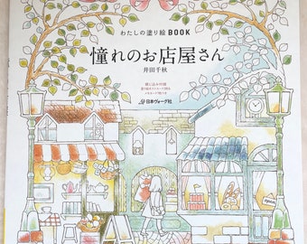 May include: A coloring book cover featuring a charming illustration of a street scene with shops and a girl walking by. The title of the book is "憧れのお店屋さん" (Akogare no O-mise-ya-san) which translates to "Dream Shops".