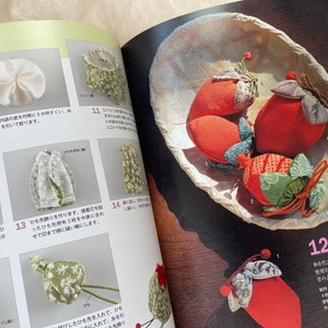 May include: Four handmade fabric柿袋 (kaki-bukuro) in the shape of persimmons. The柿袋 are made of red, green, and brown fabric with a floral pattern. The柿袋 are sitting in a woven basket.