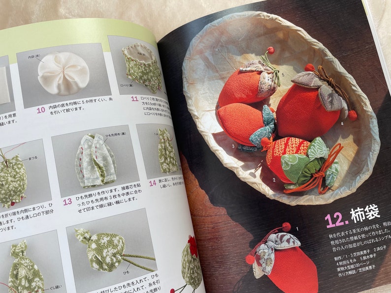 May include: Four handmade fabric柿袋 (kaki-bukuro) in the shape of persimmons. The柿袋 are made of red, green, and brown fabric with a floral pattern. The柿袋 are sitting in a woven basket.