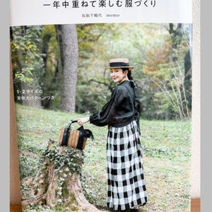 Puede incluir: Un libro de manualidades titulado BLUE BERRY JAM con una portada que muestra a una persona con sombrero de paja, blusa negra de manga larga y falda de cuadros blancos y negros, sosteniendo una cesta tejida en un bosque con texto.