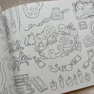 May include: A black and white illustration from a colouring book featuring Halloween-themed objects. The image includes pumpkins, candles, masks, and a cake. The word "October" is on a banner near the pumpkins.