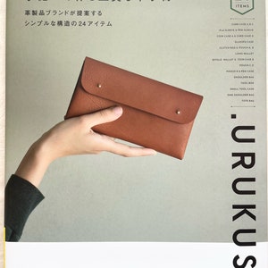 Peut inclure: Une couverture de livre avec le titre "Accessoires en cuir de haute qualité cousus à la main" en japonais. La couverture présente un portefeuille en cuir marron tenu par une main. La couverture du livre comprend également le texte "24 articles" et "URUKUST".