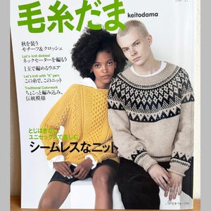 May include: A magazine cover titled Keitodama vol. 211 featuring two individuals wearing knit sweaters. One wears a textured yellow cable-knit sweater over a white collared shirt, while the other wears a beige sweater with a black geometric pattern.
