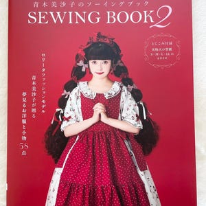 May include: A book cover with the title "MISAKO AOKI SEWING BOOK 2", featuring a woman in a red and white dress. The cover is mainly red with white text. The book is about Lolita fashion and includes patterns.