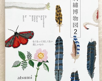 May include: A book titled "An Embroidered Book of Natural History Motifs 2" by Atsumi. The cover features colorful embroidered illustrations of a variety of natural objects, including a fish, a bird, a flower, a feather, and an insect.