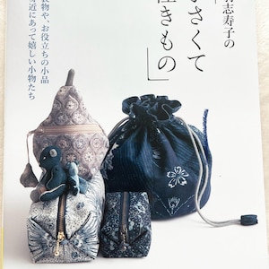 Puede incluir: Un libro titulado "Cosas pequeñas y encantadoras" con el texto japonés "黒羽志寿子の 佳きもの" que presenta una colección de pequeñas bolsas y estuches hechos a mano en tela azul y blanca con motivos florales. La portada del libro presenta un primer plano de las bolsas y estuches.