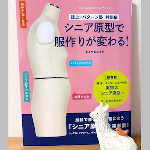 Könnte beinhalten: Ein japanisches Buch, "Senior Pattern und Dressmaking Changes!", mit rosa und weißem Einband. Das Bild zeigt eine Schneiderpuppe und eine weiße Lama-Figur. Der Text ist auf Japanisch, mit etwas englischem Text.