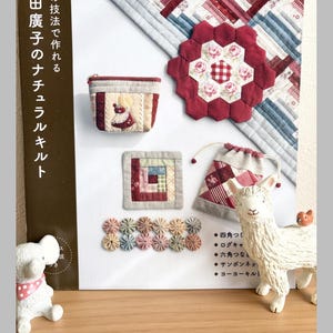 Puede incluir: Una colección de edredones y accesorios hechos a mano, que incluyen un pequeño monedero, un posavasos y una bolsa con cordón. Los artículos presentan telas rojas, blancas y azules con estampados florales y geométricos. También se ve un libro con texto japonés.