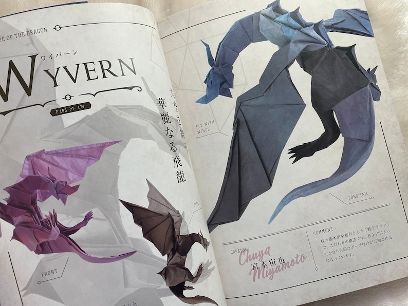 May include: A book page with a blue origami wyvern with a long tail and wings. The text on the page reads "Fly with Wises" and "Long Tail". The creator is listed as "Chuya Miyamoto".