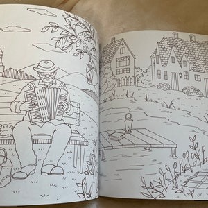 Puede incluir: Una doble p&aacute;gina de un libro para colorear con dibujos lineales detallados. Una p&aacute;gina muestra a un hombre tocando el acorde&oacute;n en un banco del parque con un gato y una bolsa. La otra p&aacute;gina representa casas, un lago y un picnic.
