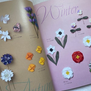 May include: A book with origami flower instructions. The book has a pink background with the word "Winter" written in black. The book also has a brown background with the word "Autumn" written in black. The book features origami flowers in various colors, including white, red, purple, and yellow.
