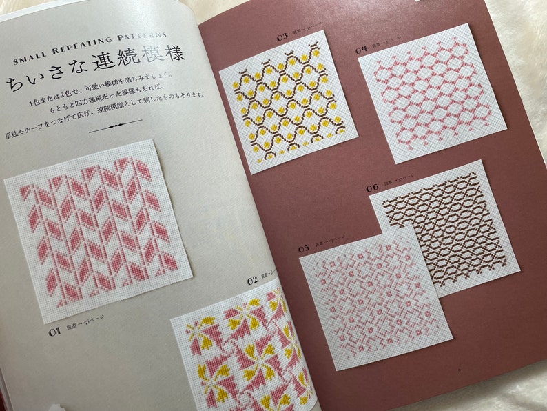 May include: A book with a pink cover and white pages. The book features a variety of small repeating patterns in pink, yellow, and brown. The title of the book is "Small Repeating Patterns" and the subtitle is "ちいさな連続模様".