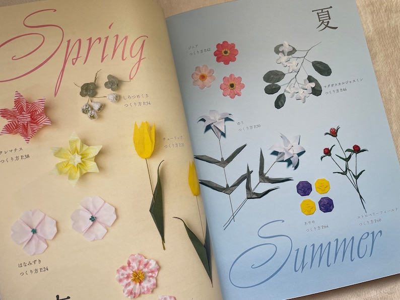 May include: A book with origami flower designs. The left page shows spring flowers, including a red origami star, a yellow origami tulip, and a pink origami flower. The right page shows summer flowers, including a white origami jasmine, a white origami lily, and a purple origami flower.