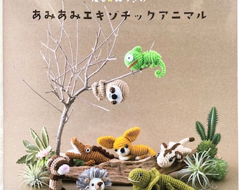 Puede incluir: Un libro titulado "Amigurumi Kitchen" con una estrella amarilla y el texto "Amigurumi para principiantes" en japonés. La portada presenta una variedad de figuritas de animales de crochet, incluyendo un camaleón, un perezoso, un chihuahua, un cocodrilo, un erizo, un hurón y un lagarto, todos dispuestos en una rama de madera y rodeados de pequeñas plantas.