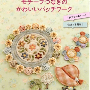 Op de afbeelding: Een boekomslag met een bloemenmotief en de titel "モチーフつなぎのかわいいパッチワーク" (Schattig patchwork met verbonden motieven) in het Japans. De boekomslag bevat ook de tekst "南久美子の" (Kumiko Minami's) en "レティフティックシリース" (Letiff Tick Series) in het Japans. De boekomslag toont een verscheidenheid aan kleurrijke stoffen bloemen en een bloemenpatroon.