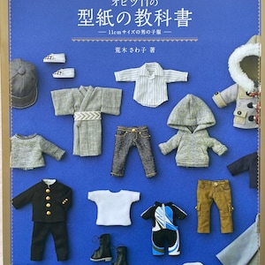 May include: A book cover with a blue background and the title "Obitsu 11's Pattern Textbook - 11cm sized boy's clothes -" in Japanese. The cover features a variety of miniature clothing items for a doll, including a white shirt, a blue jacket, a pair of jeans, and a grey sweater.