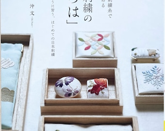 May include: A book titled "Japanese Embroidery: "いろは"" with a white background and a close-up of several small wooden boxes containing embroidered fabric samples. The book cover features Japanese text and the title "いろは" in large, bold letters.