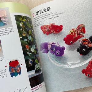 May include: A close-up of a book page showing a craft project for making small fabric goldfish. The page is titled "9. 出目金袋" and shows several finished goldfish in different colors and patterns. The goldfish are made from fabric scraps and have small black eyes. The page also includes instructions for making the goldfish.