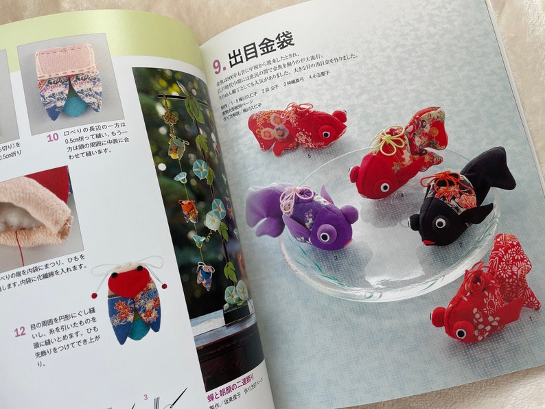 May include: A close-up of a book page showing a craft project for making small fabric goldfish. The page is titled "9. 出目金袋" and shows several finished goldfish in different colors and patterns. The goldfish are made from fabric scraps and have small black eyes. The page also includes instructions for making the goldfish.