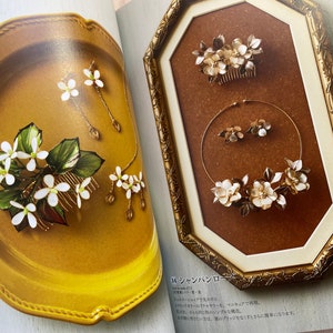 May include: Two sets of white flower hair accessories with gold accents. The first set is a comb with a cluster of flowers and leaves. The second set is a necklace and earrings with a similar design. The text in the image reads "シャンパンロゼ".
