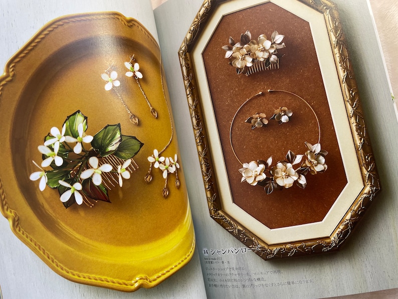 May include: Two sets of white flower hair accessories with gold accents. The first set is a comb with a cluster of flowers and leaves. The second set is a necklace and earrings with a similar design. The text in the image reads "シャンパンロゼ".
