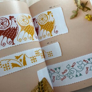 May include: A book with cross-stitch patterns featuring a rooster, a floral design, and a fish design. The book has page numbers 60, 61, and 62.