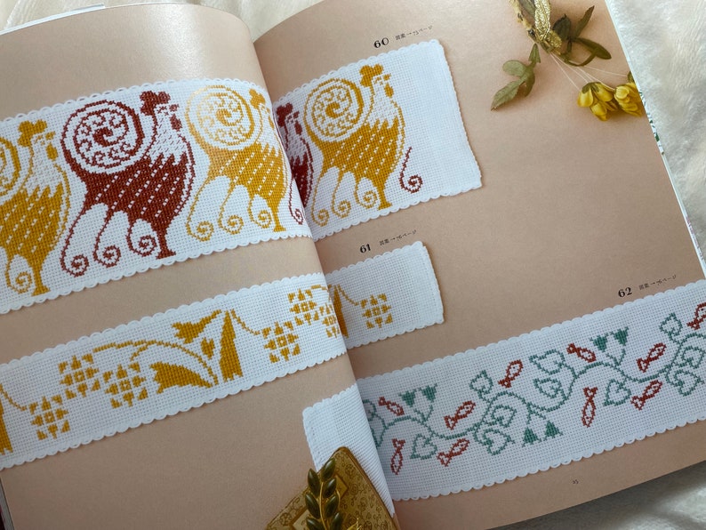 May include: A book with cross-stitch patterns featuring a rooster, a floral design, and a fish design. The book has page numbers 60, 61, and 62.