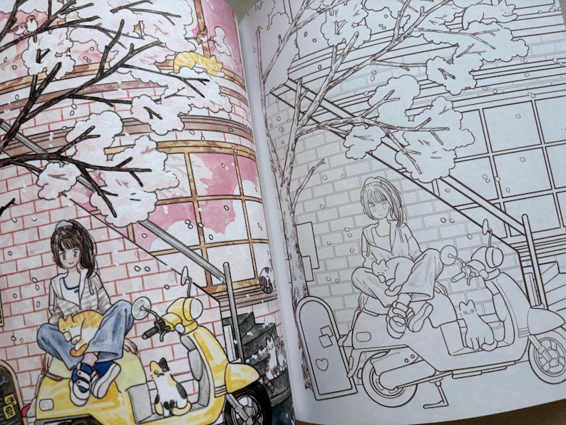 May include: An open colouring book featuring two pages with identical line art illustrations. The left page is partially coloured with a yellow scooter, a person, and cats under a tree. The right page shows the same scene in black and white outlines.