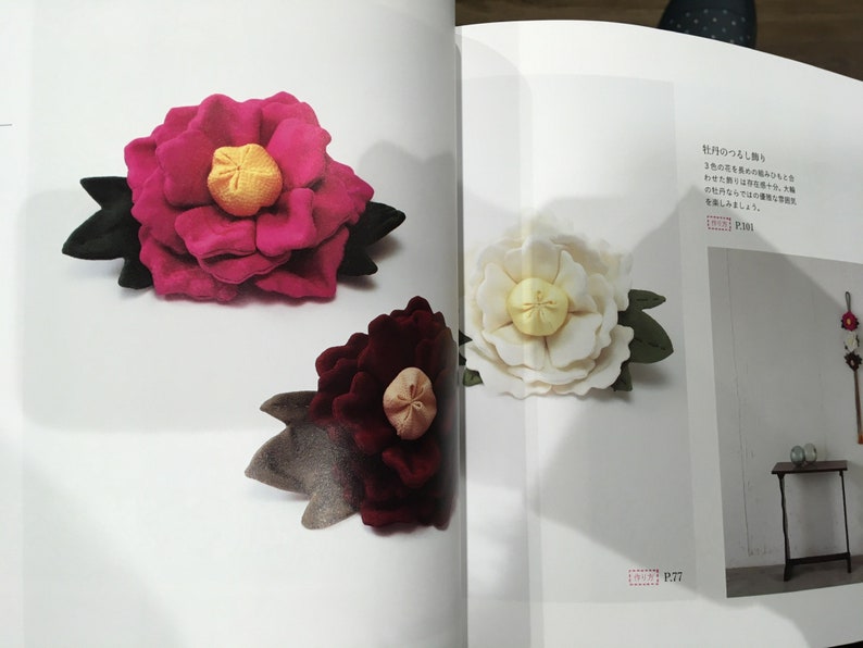 May include: Three fabric flowers, two pink and one white, with yellow centers and green leaves. The flowers are arranged on a white background with text in Japanese.