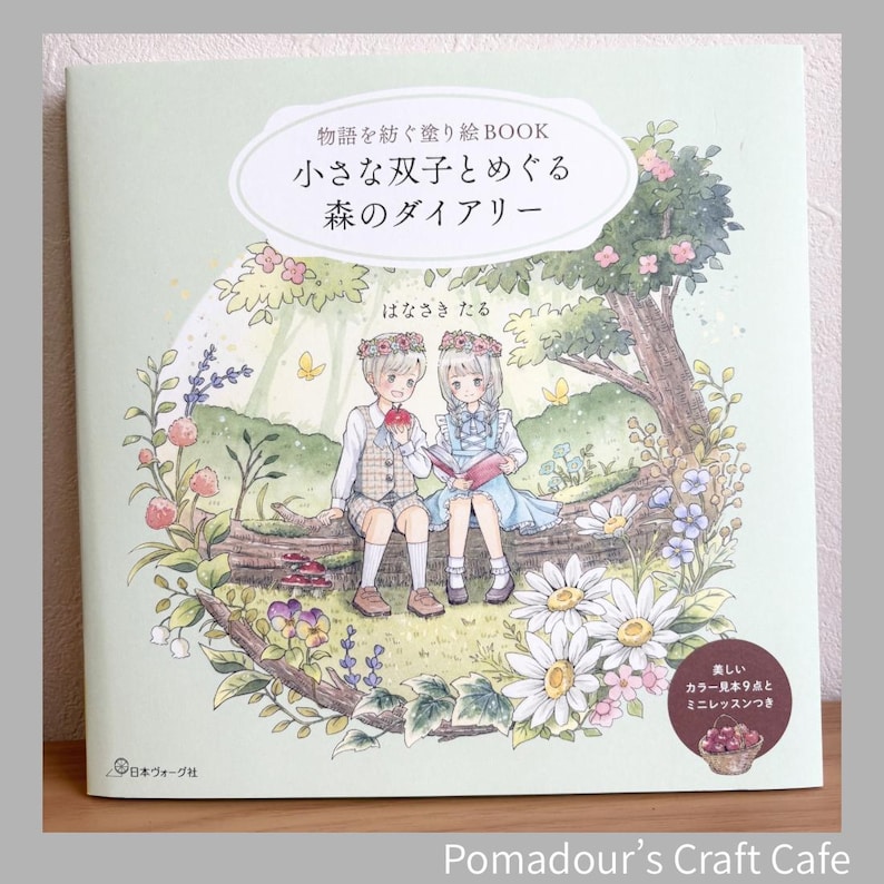 Pu&ograve; includere: Un libro da colorare con copertina morbida con una copertina verde chiaro con un'illustrazione di due bambini in un ambiente forestale. Il titolo del libro &egrave; in giapponese, con testo aggiuntivo e illustrazioni floreali. Il libro &egrave; su una superficie di legno.