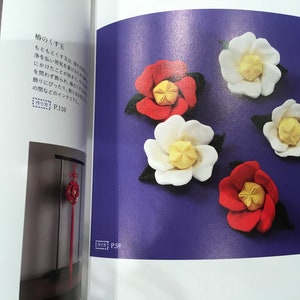 May include: Five felt flower decorations in red and white with yellow centers. The flowers are arranged on a purple background. The text "椿のくす玉" is visible in the top left corner of the image. The text "作り方 P.110" is visible in the bottom left corner of the image. The text "P.59" is visible in the bottom right corner of the image.