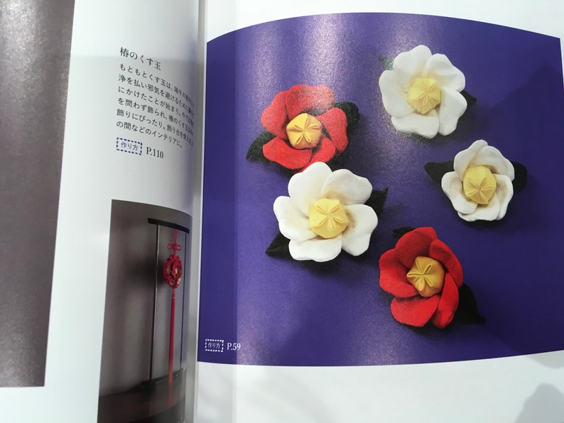 May include: Five felt flower decorations in red and white with yellow centers. The flowers are arranged on a purple background. The text "椿のくす玉" is visible in the top left corner of the image. The text "作り方 P.110" is visible in the bottom left corner of the image. The text "P.59" is visible in the bottom right corner of the image.
