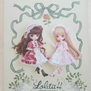 Könnte beinhalten: Ein Zeitschriften-Cover mit zwei Puppen in rosa und weißen Kleidern, Hauben und langen Haaren. Auf dem Cover steht "Dollybird vol.40" und "Lolita!!", mit dekorativen Bändern, Rosen und Schwänen. Das Magazin stammt von Pomadour's.