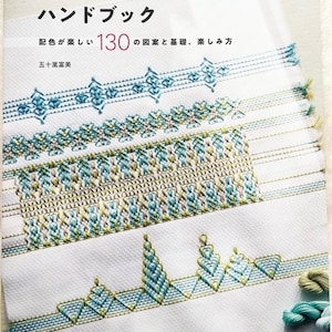 Può includere: Copertina di un libro con il titolo "Manuale di ricamo svedese" in giapponese. La copertina presenta uno sfondo bianco con disegni di ricamo colorati in tonalità di verde, blu e marrone. Il testo "130" è visibile nell'angolo in alto a sinistra della copertina.