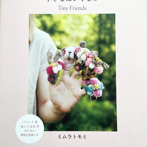 Può includere: Copertina di un libro con il titolo "Tiny Friends" in inglese e giapponese. L'immagine presenta piccoli animali di peluche fatti a mano e colorati. Il libro include anche le istruzioni per realizzare i giocattoli.