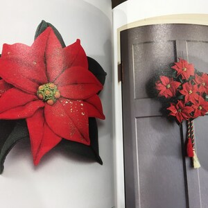 May include: A red felt poinsettia flower with green leaves. The flower is decorated with gold glitter. The flower is shown on a white background.