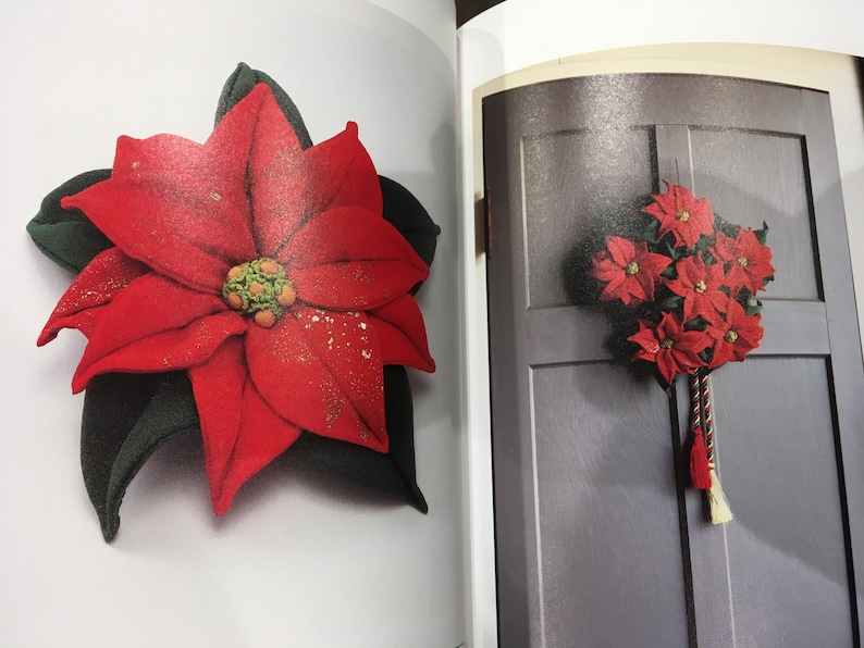 May include: A red felt poinsettia flower with green leaves. The flower is decorated with gold glitter. The flower is shown on a white background.
