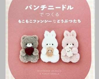 May include: A craft book cover with a pink oval center featuring three fuzzy animal figures: a grey bear holding a red heart, a white rabbit holding a small brown bear, and a light pink rabbit holding a small white bear. Text includes "mocomoco march", "パンチニードルでつくるもこもこファンシーなどうぶつたち", "MOCOMOCO ANIMALS & PUNCH NEEDLE", and "KADOKAWA".