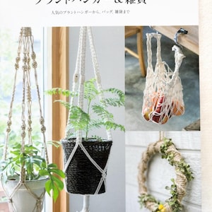 May include: A book cover showcasing macrame plant hangers and accessories. The image displays macrame plant hangers with plants, a macrame bag filled with fruit, and a decorative wreath. The cover text reads "Macrame Plant Hanger & Zakka", with Japanese text above.