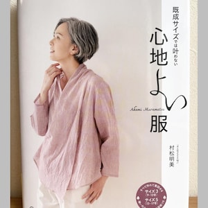 May include: A book cover featuring a woman wearing a pink wrap top and white pants. The book title is in Japanese characters, with the author's name and the words "Heart Warming Life Series" visible. The book cover also has text in Japanese.
