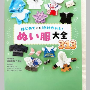 May include: A collection of miniature doll clothes, including a shark hoodie, sailor outfit, and formal wear, arranged on a green background. The image features the text "ぬい服大全 313" and "Pomadour's".