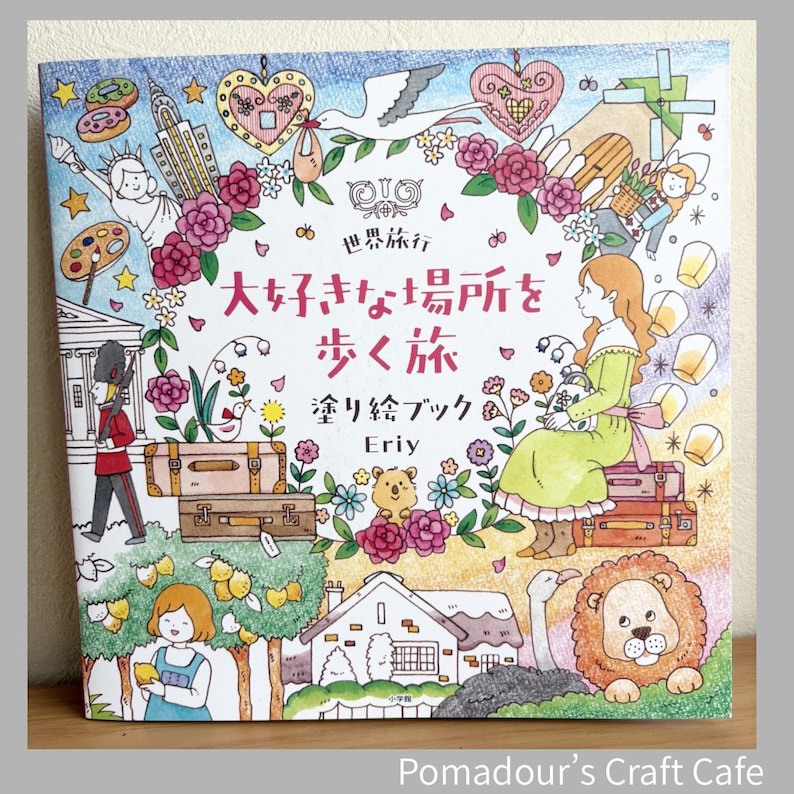 May include: A square coloring book with a colorful illustration. The cover features a woman in a green dress, suitcases, and various drawings of landmarks and animals. Japanese text is visible. The book is titled "Eriy" and is from "Pomadour's Craft Cafe."