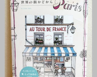May include: A coloring book titled Storefront Coloring Book Paris featuring a line drawing of a French cafe with a blue and white striped awning, a sign reading Au Tour De France, and a light blue circular sticker with Japanese text.
