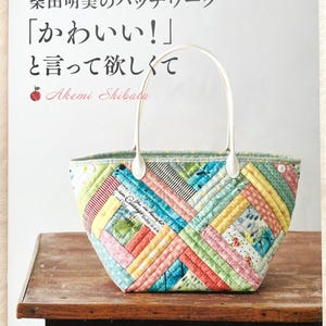 May include: A patchwork tote bag with white handles, featuring a variety of fabric patterns in blue, pink, yellow, and green. The bag is on a wooden surface. Japanese text is visible on the book cover.