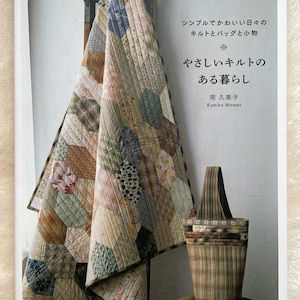 May include: A book titled "やさしいキルトのある暮らし" by 南 久美子 (Kumiko Minami) featuring a quilt and a bag made from patchwork fabric. The book cover is a light brown color with a white background and the title is written in Japanese.