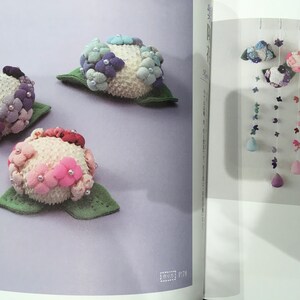 May include: Three felt flower embellishments in shades of pink, purple, and blue. The flowers are arranged on a light purple background. The flowers are made of felt and have a textured surface. The flowers are surrounded by green felt leaves.